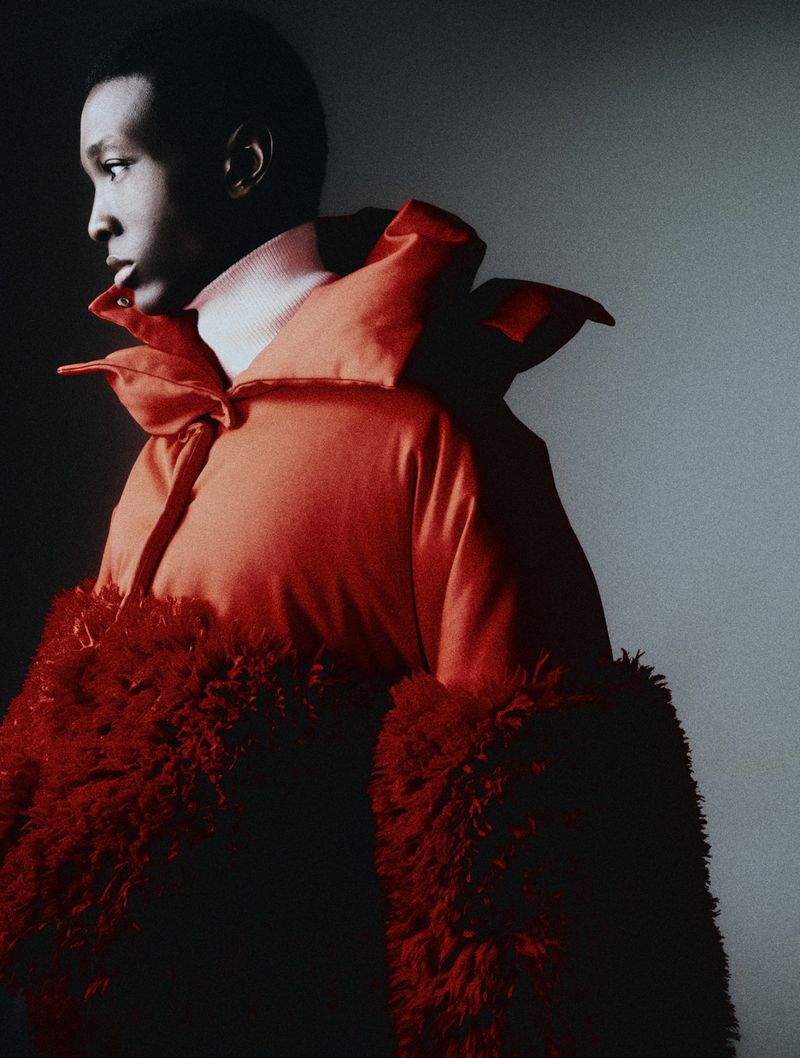 Fashionable Black model in a red puffer jacket with fur sleeves poses in a studio with soft lighting.