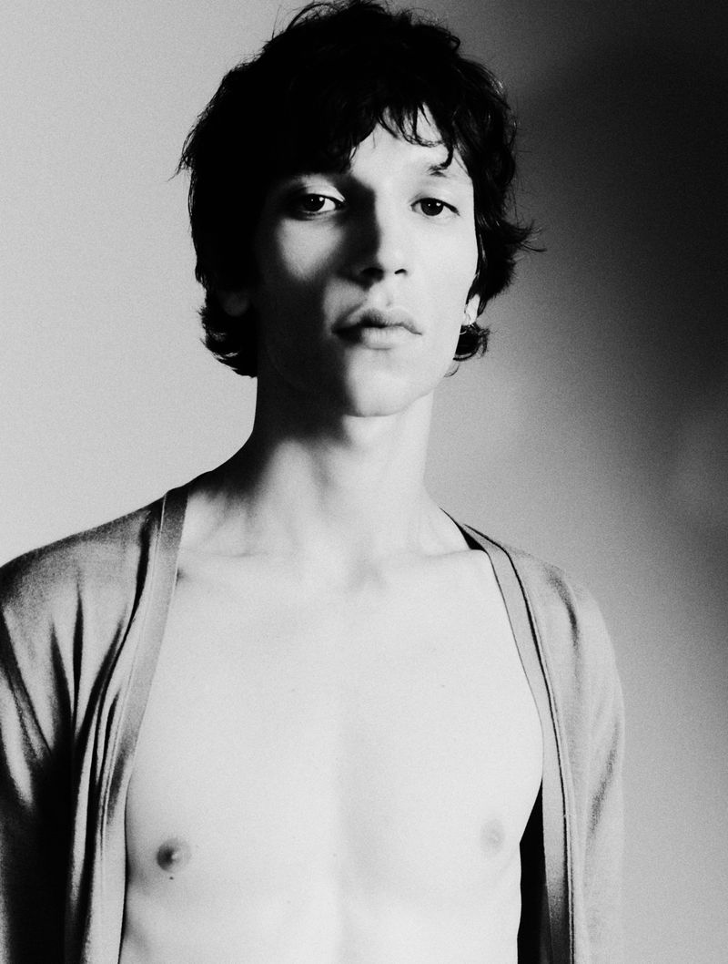 Black and white portrait of a young adult male with dark hair, wearing a cardigan, posing indoors with a neutral expression.