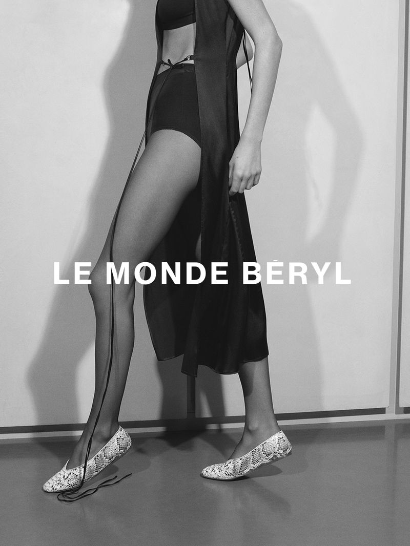 Model in black wrap skirt and patterned flats posing against a light background with visible shadows