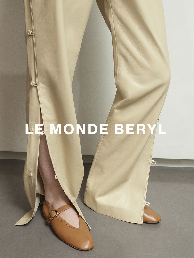 Close-up of cream trousers with side button slits and tan leather Mary Jane shoes against a neutral background.