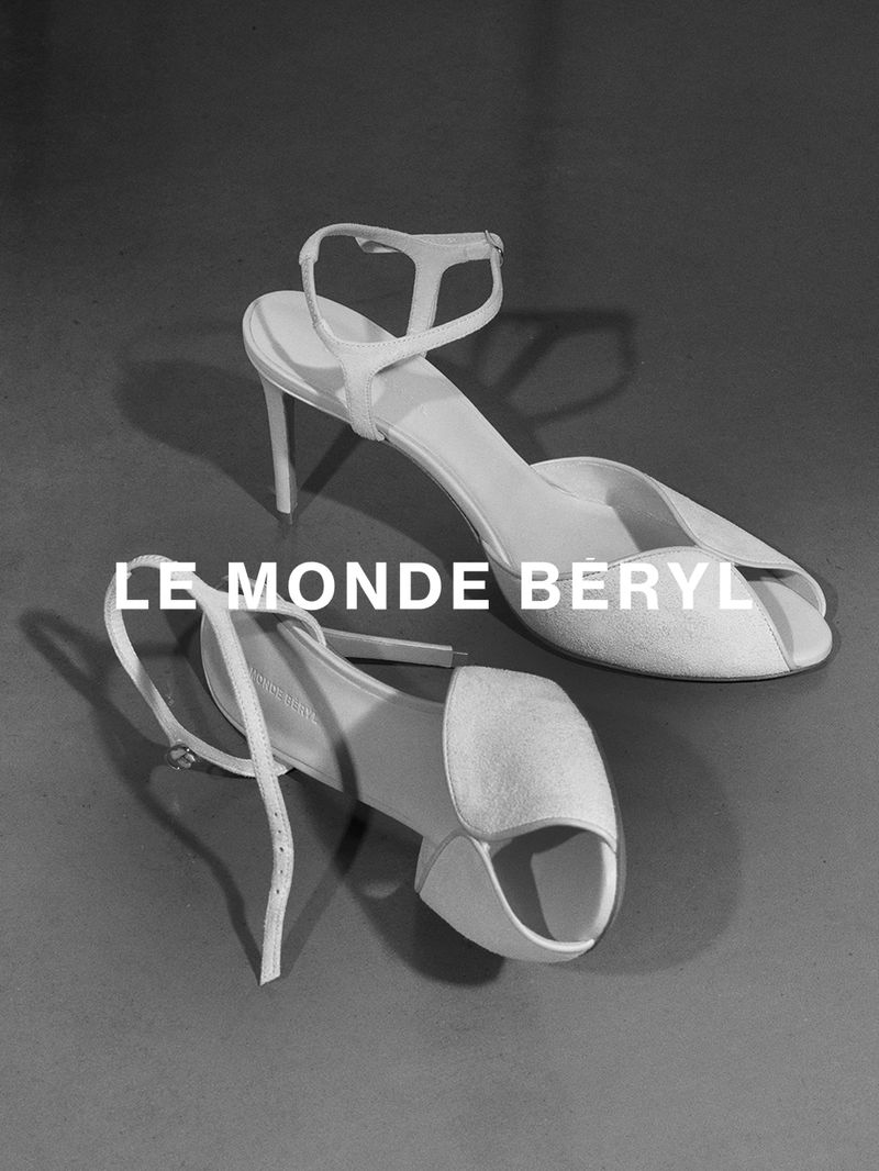 Monochrome product shot of two elegant high-heeled sandals on a dark surface with bold brand typography overlaid.
