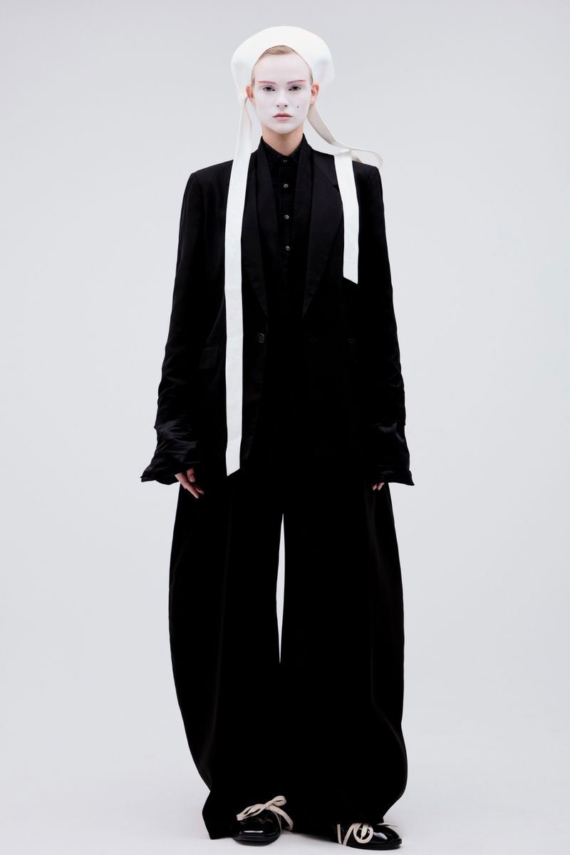 Model in black suit and white hat with long ribbons against a seamless white background for Vogue Czechoslovakia editorial