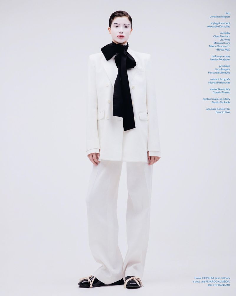 Model wearing a white suit and black bow tie standing against a white seamless background