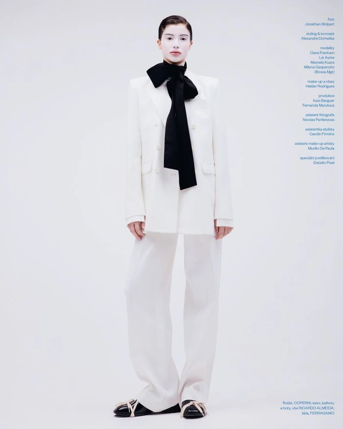 Model wearing a white suit and black bow tie standing against a white seamless background