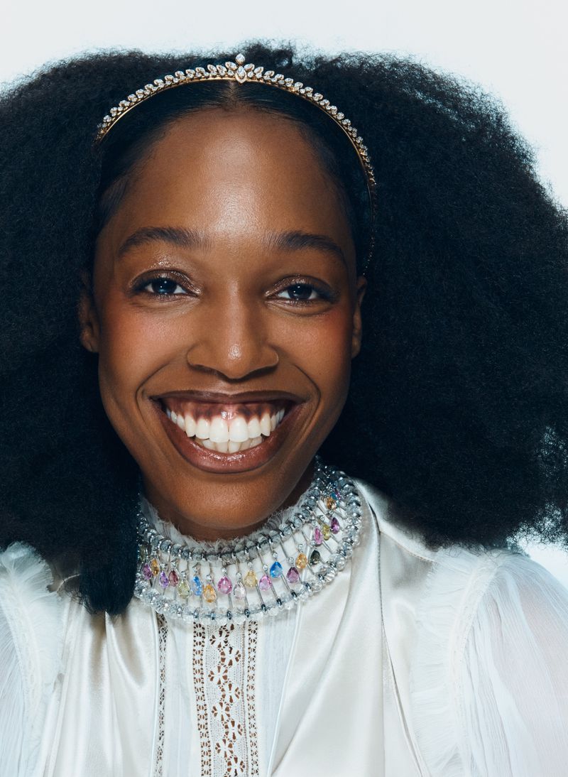 Portrait of Black woman wearing a jewelled tiara and beaded choker necklace against a white background