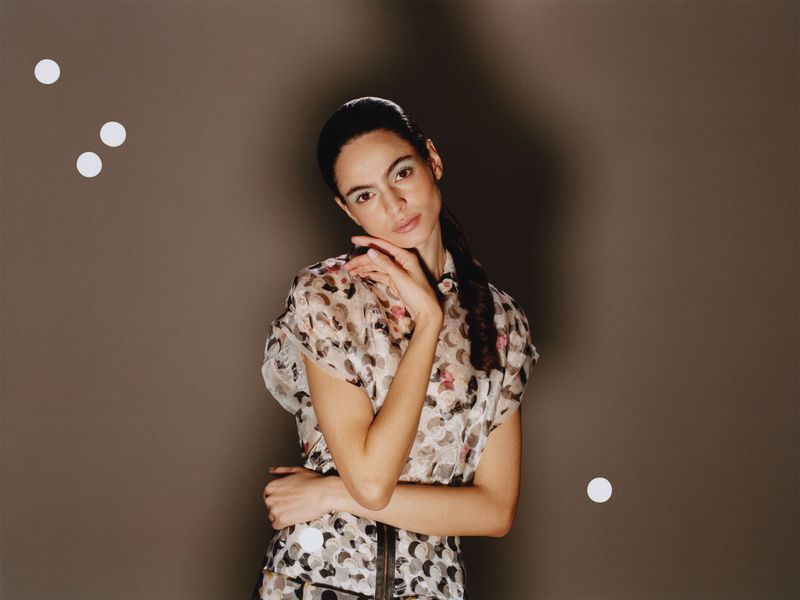 Model in patterned blouse with hand to chin against a grey backdrop for Family Style
