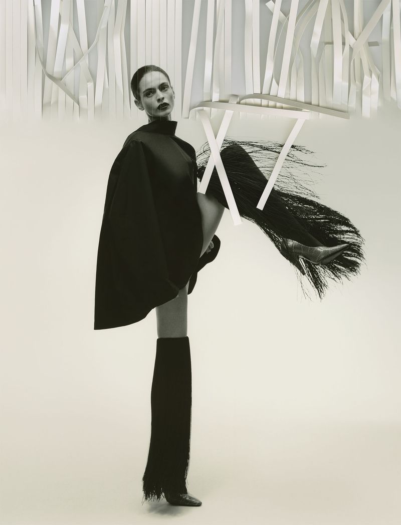 Model in dark cape and fringed boots posing beneath hanging white ribbons for Family Style Summer 2026