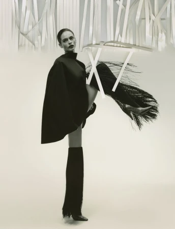 Model in dark cape and fringed boots posing beneath hanging white ribbons for Family Style Summer 2026