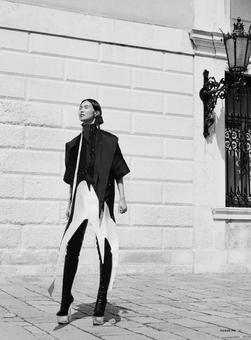 Model in architectural monochrome outfit with platform boots standing against a classical stone building exterior.