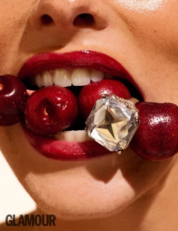 Extreme close-up of a person holding glossy red cherries and a large diamond ring between their lips for Glamour Bulgaria.