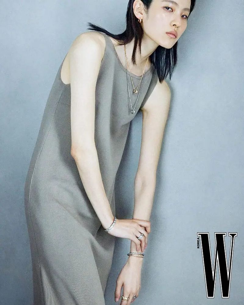 Model Song Ah Woo wearing a grey sleeveless dress and layered necklaces against a textured grey background for W Korea.