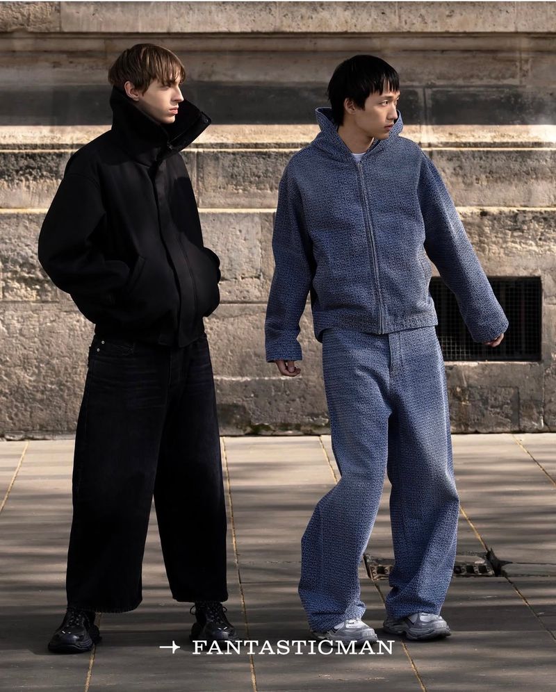 Two male models posing outdoors in front of a stone building, wearing textured casual jackets and trousers.