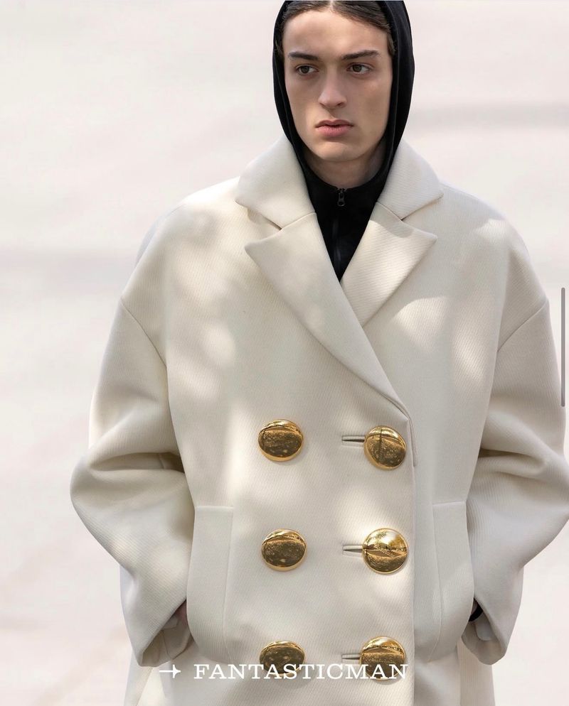 Model wearing a white double-breasted coat with large gold buttons and a black hooded top underneath.
