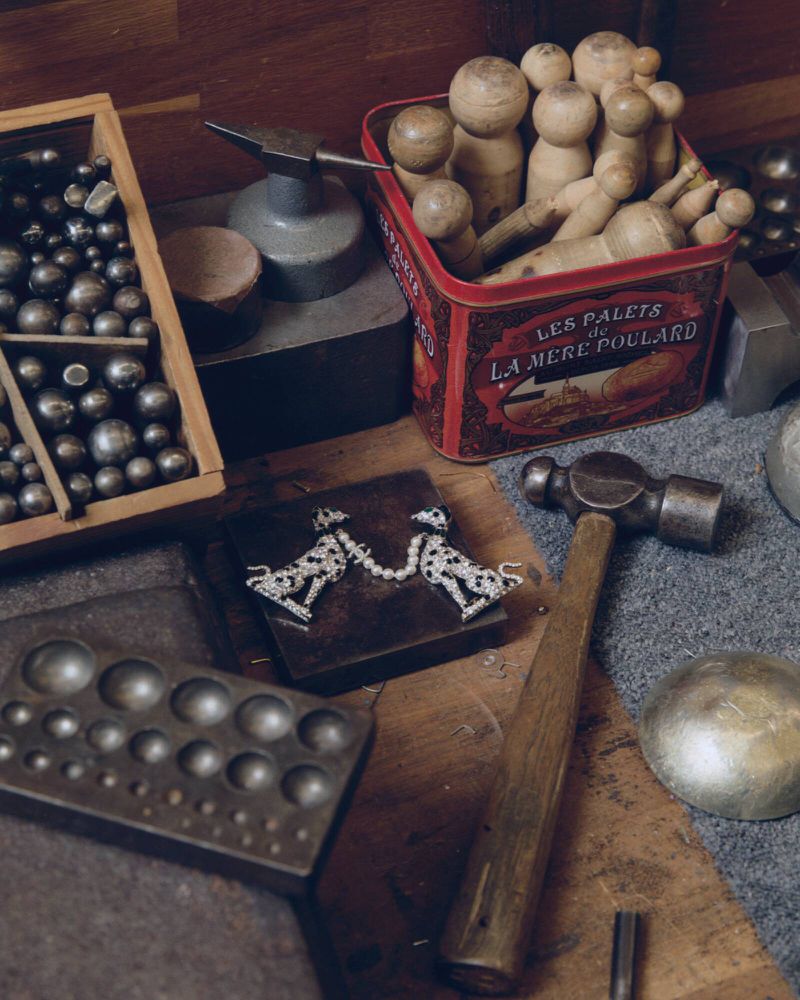 High-angle still life of artisan jewelry workbench with metalworking tools, hammer, wooden stakes, and animal brooches.