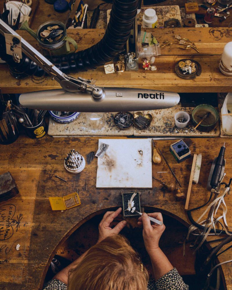 Overhead view of a jeweler working at a wooden workbench filled with tools, specialized equipment, and small components.