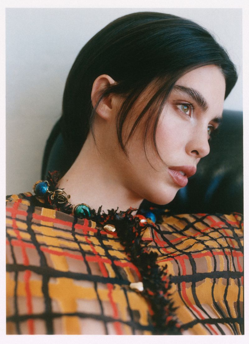 Close-up portrait of a woman wearing a yellow plaid patterned top and a beaded gemstone necklace.
