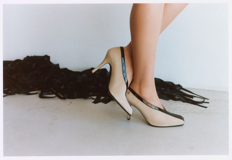 Close-up of a model standing in two-tone high heels against a plain white studio background with dark ribbons