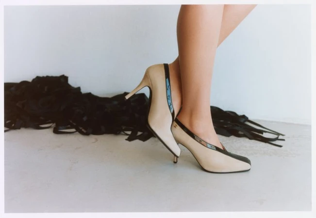 Close-up of a model standing in two-tone high heels against a plain white studio background with dark ribbons