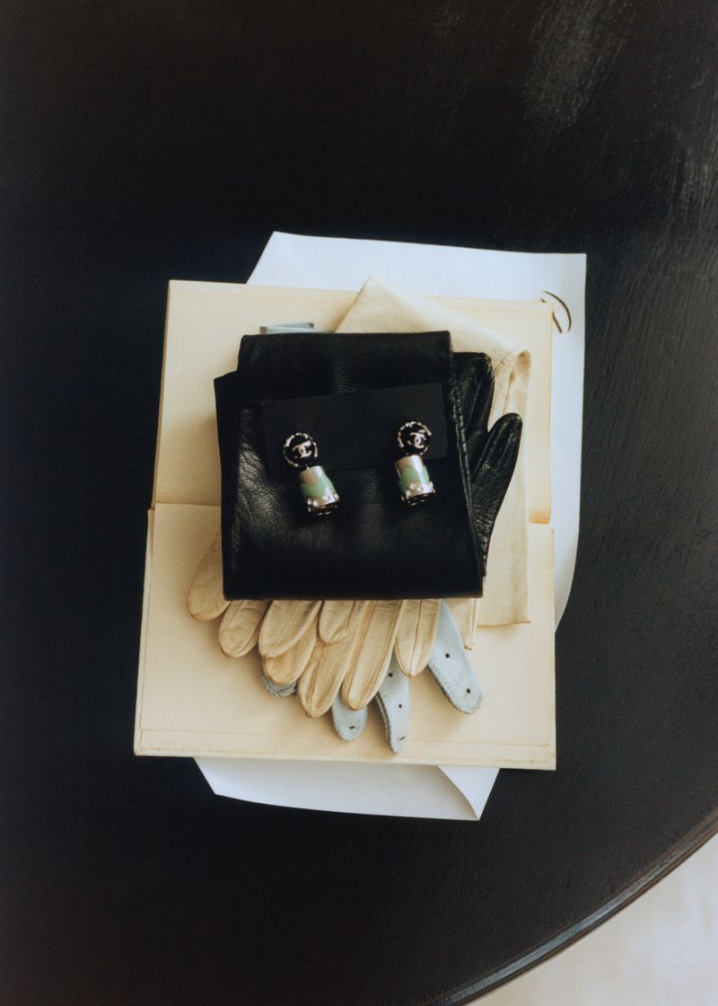 Overhead flat lay of black leather gloves and cream gloves resting on top of a book and paper on a dark surface.