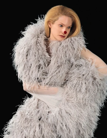 Model wearing a voluminous grey feather boa and a red nose against a solid black background.