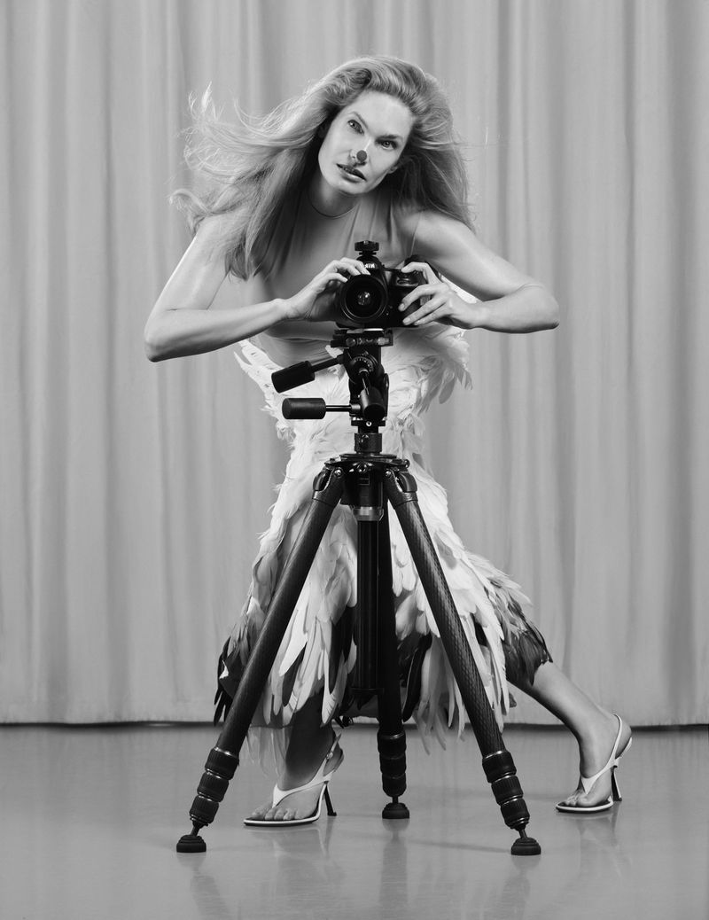 Monochrome fashion portrait of a model holding a camera on a tripod in a studio setting
