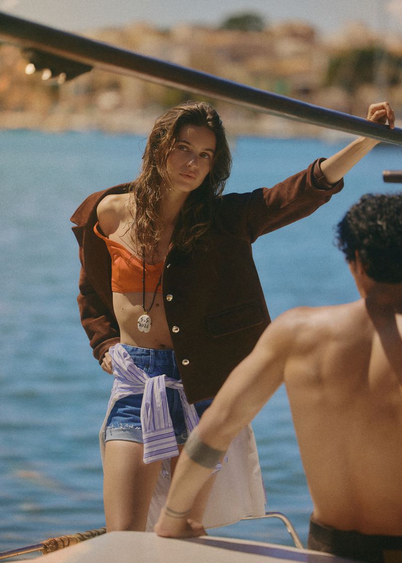 Woman in brown jacket and denim shorts standing on a boat with a man in the foreground, shot for Elle France