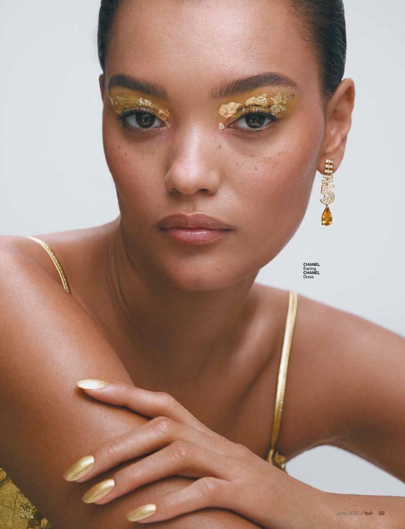 Close-up beauty shot features a female model with golden eye makeup, tan skin, and gold manicure, highlighting fashion and cosmetic artistry.