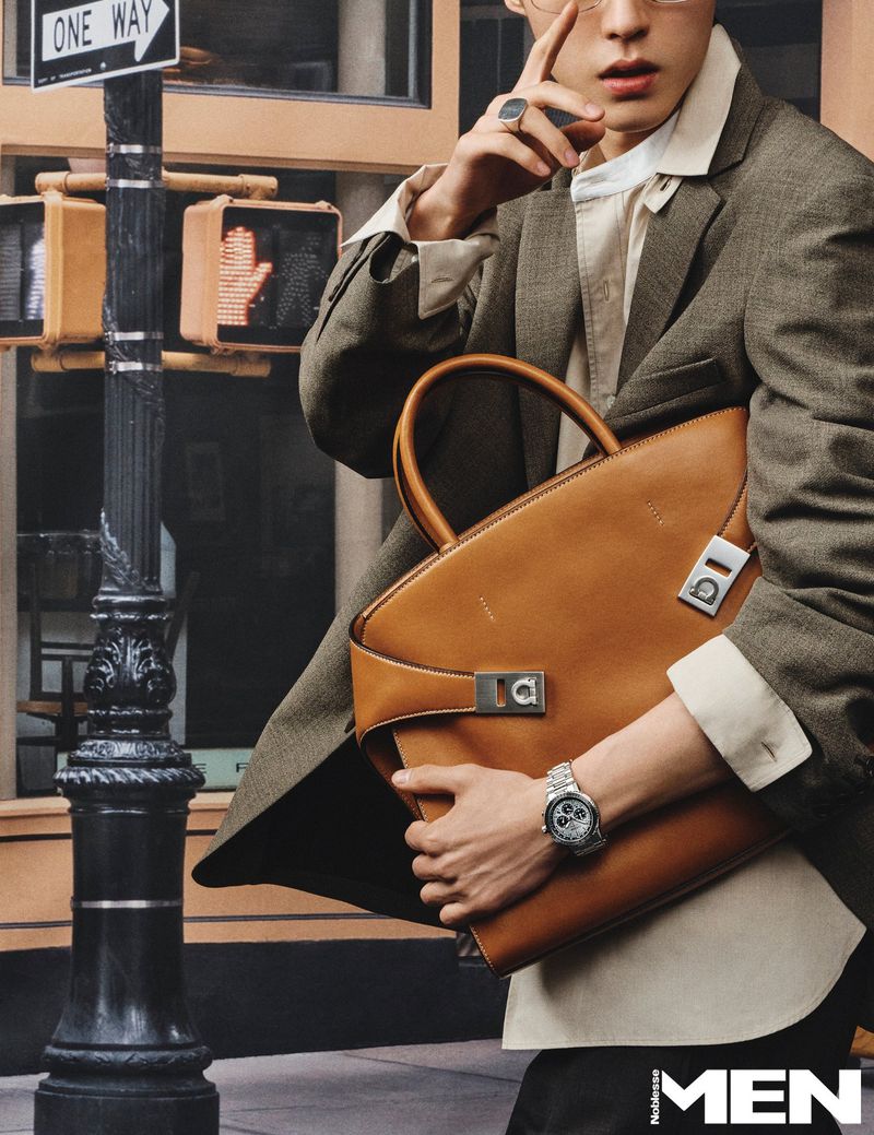 Man wearing a green blazer and holding a large tan leather handbag outdoors near a street sign.
