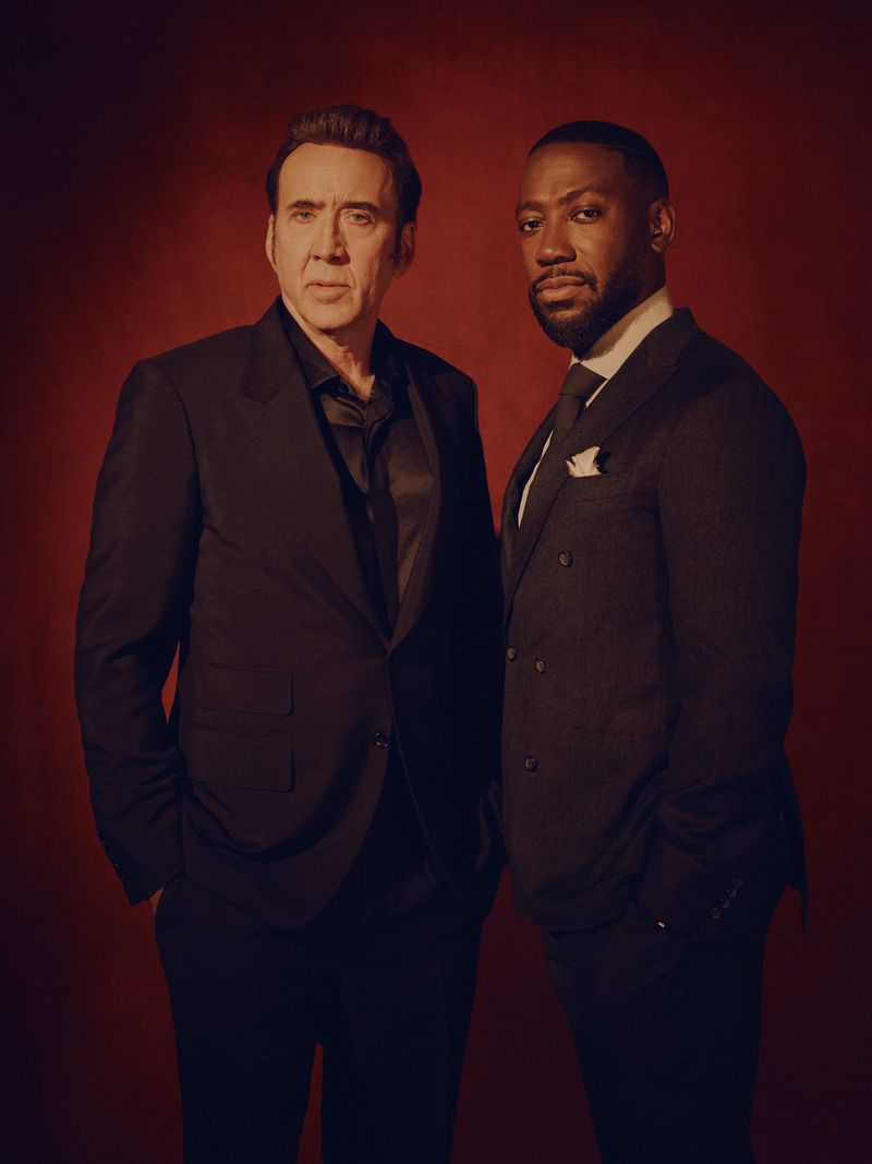 Portrait of Nicolas Cage and Lamorne Morris wearing black suits standing against a red backdrop for LA Times by David Urbanke