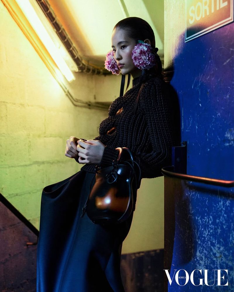 Model Song Ah Woo leaning against a wall wearing a dark textured top and holding a dark handbag in a stairwell