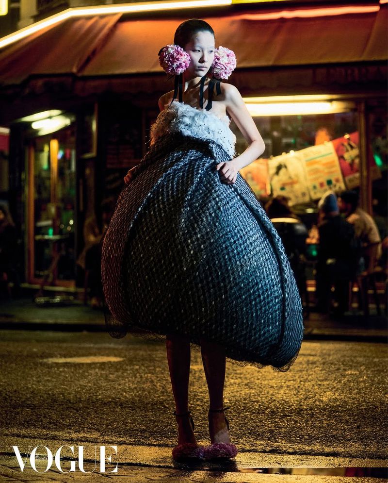 Model wearing a voluminous sculptural dress and large pink floral ear pieces on a city street at night for Vogue Korea.