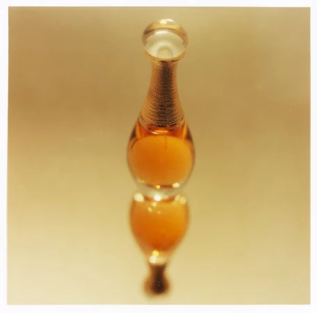 Amber perfume bottle with a golden neck and rounded stopper standing vertically on a reflective surface
