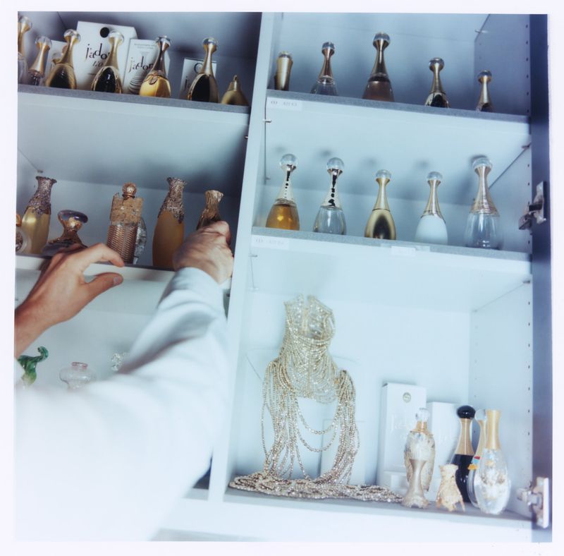 Close-up of hands arranging luxury perfume bottles and display items on shelves inside a cabinet, shot for ODDA Magazine