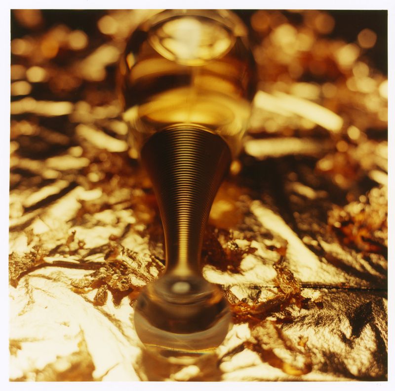Close-up macro shot of a perfume bottle neck and cap resting on a shimmering golden metallic foil surface.