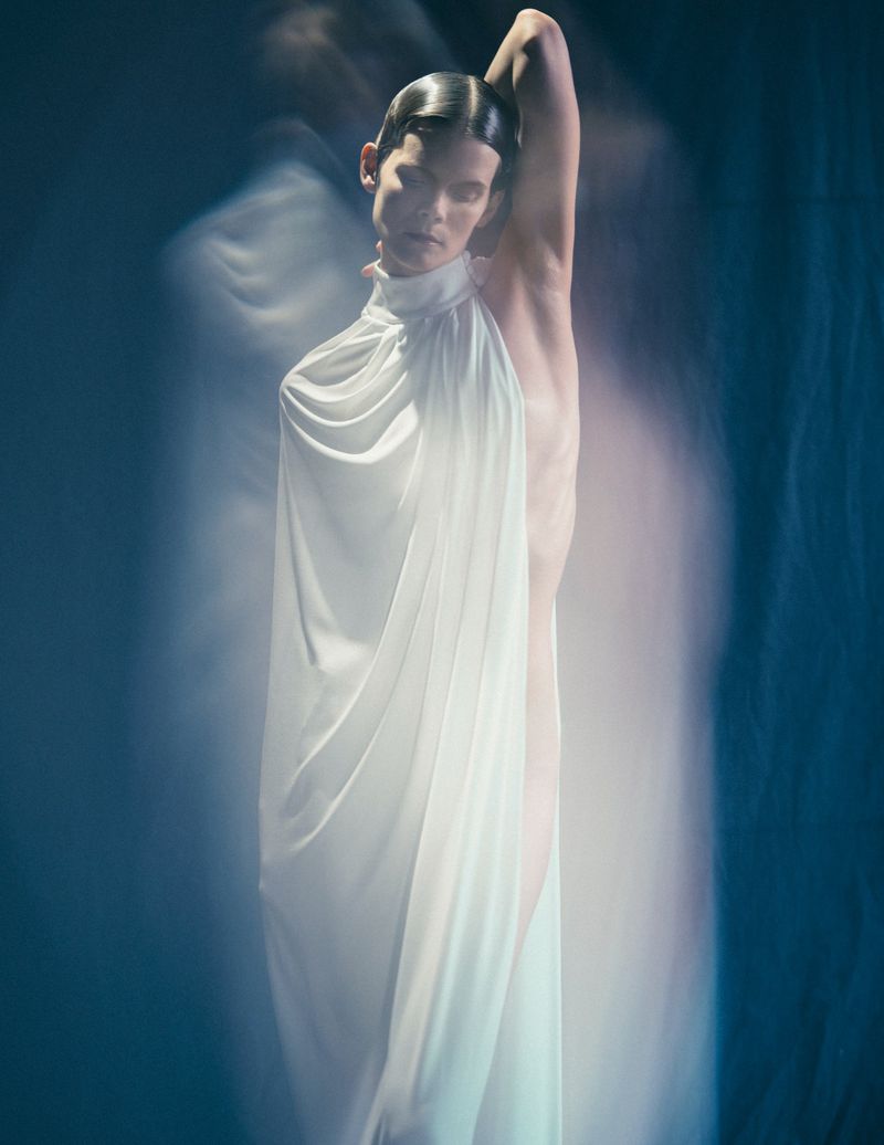Model Irina Kravchenko wearing a flowing white halter dress in a surreal editorial portrait for Manifeste du Surrealisme by L'Officiel Italia.