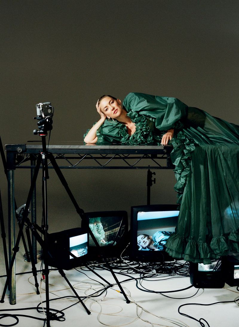 Kate Hudson lying on a table in a ruffled green gown surrounded by television monitors and camera gear