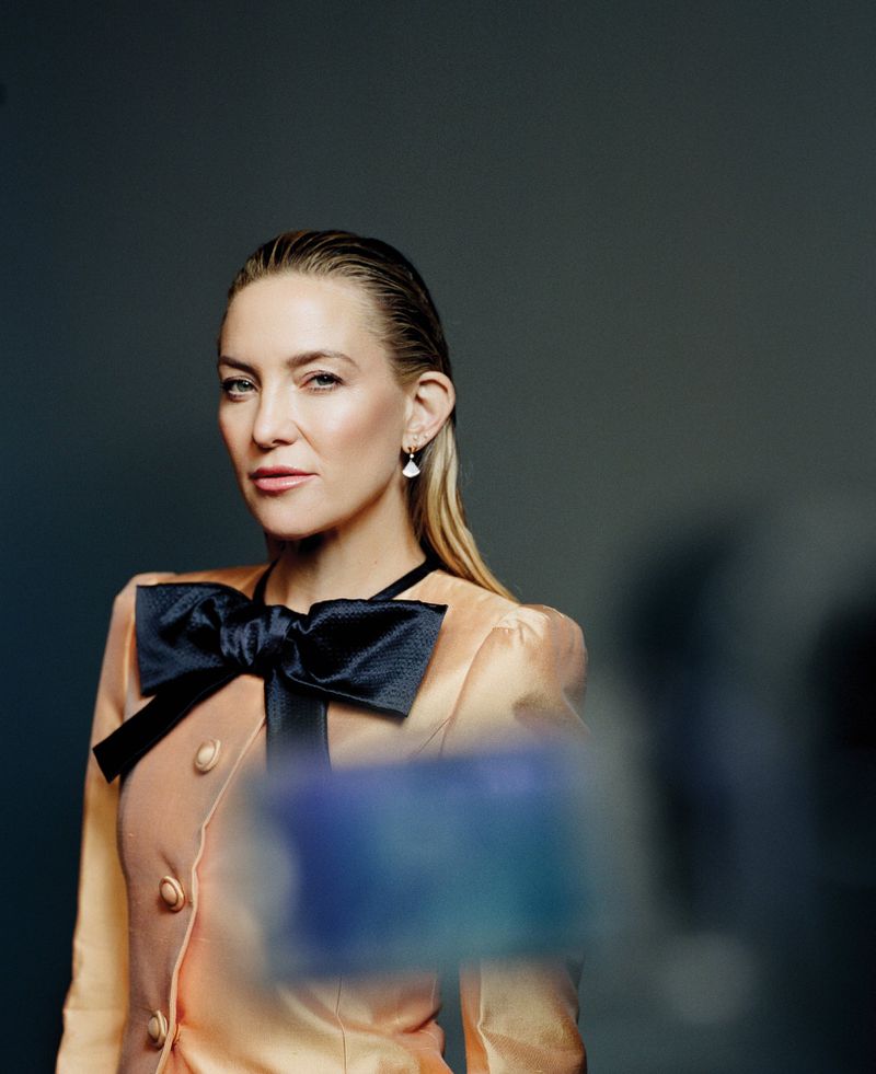 Kate Hudson wearing peach jacket with large black bow against dark grey studio backdrop for L'Officiel Italia.