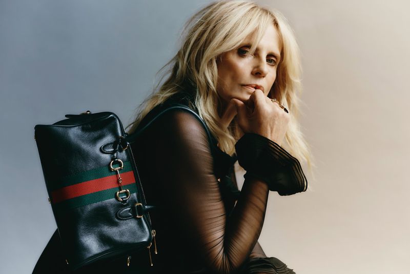 Blonde woman wearing sheer black top resting chin on hand with dark leather handbag for L'Officiel Italia isabella ferrari project