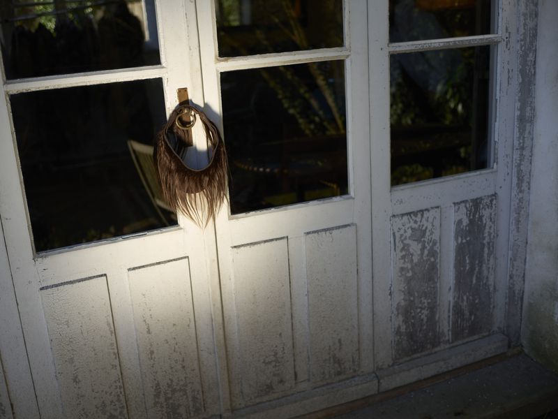 Fringed textile accessory hanging from a white painted multi-paneled door, casting a long shadow in bright sunlight.