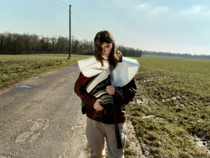 Margaux Martin standing on a rural road wearing a brown leather jacket, oversized white collar, and beige trousers for Exhibition Magazine.