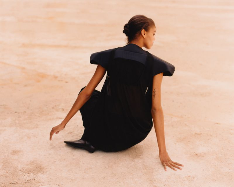 Model wearing a structured black top seated on a sandy terrain for Present Space editorial.