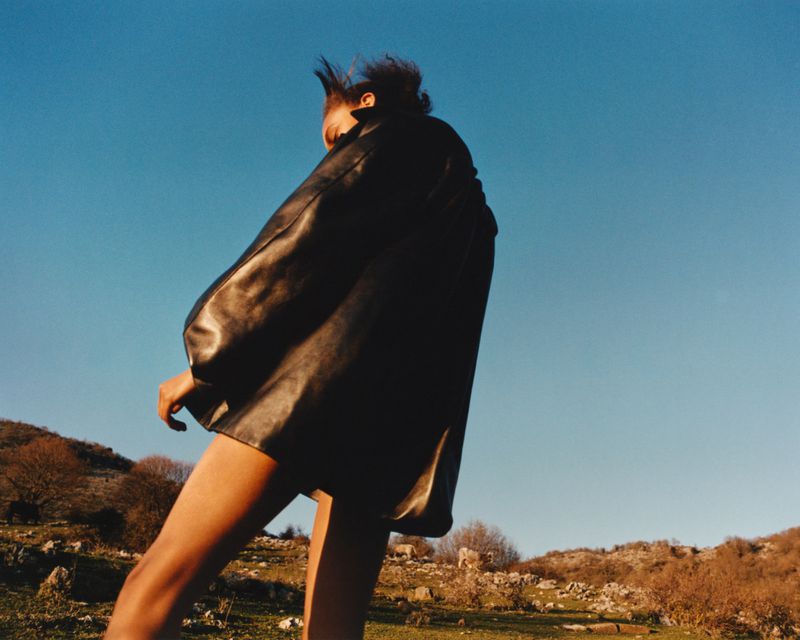 Model wearing a black leather jacket against a clear blue sky and a hilly landscape for the Present Space project by Andrew Jacobs.