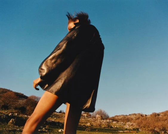 Model wearing a black leather jacket against a clear blue sky and a hilly landscape for the Present Space project by Andrew Jacobs.