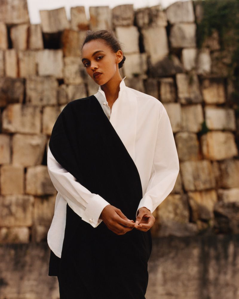 Model wearing a structured black and white shirt against a textured stone block wall for Present Space project.
