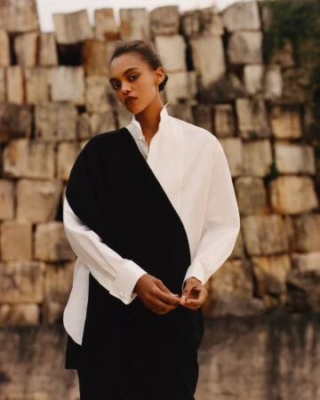 Model wearing a structured black and white shirt against a textured stone block wall for Present Space project.