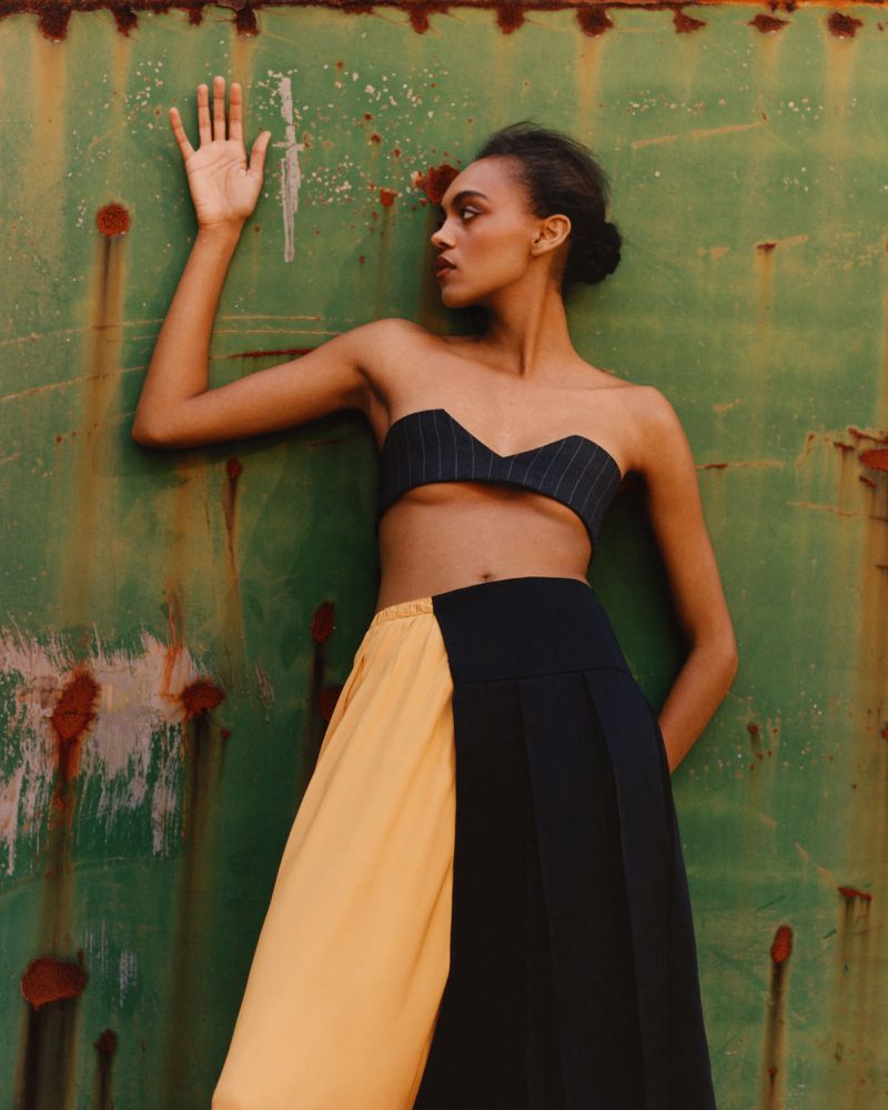 Model Bebe Parnell leaning against a weathered green metal wall for the Present Space project