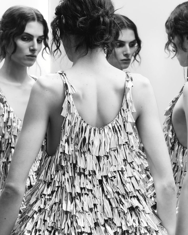 Model in reflective fringed dress captured through multiple mirror reflections in a black and white fashion editorial.