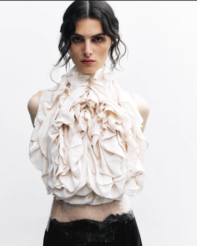 Model wearing a heavily ruffled white top against a clean white studio background for Exhibition Magazine.