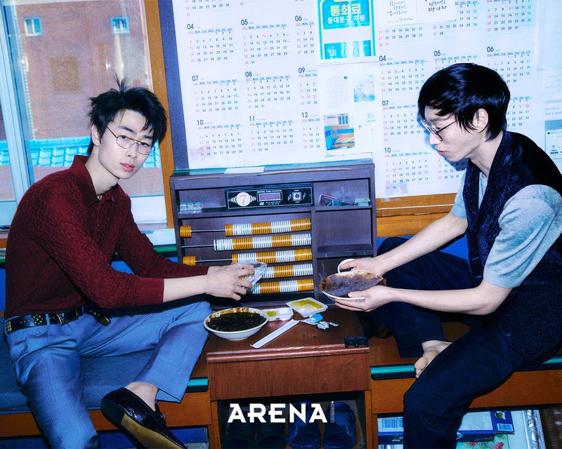 Two men sitting in an office space with a large wall calendar holding bowls of food for Arena Homme Korea project
