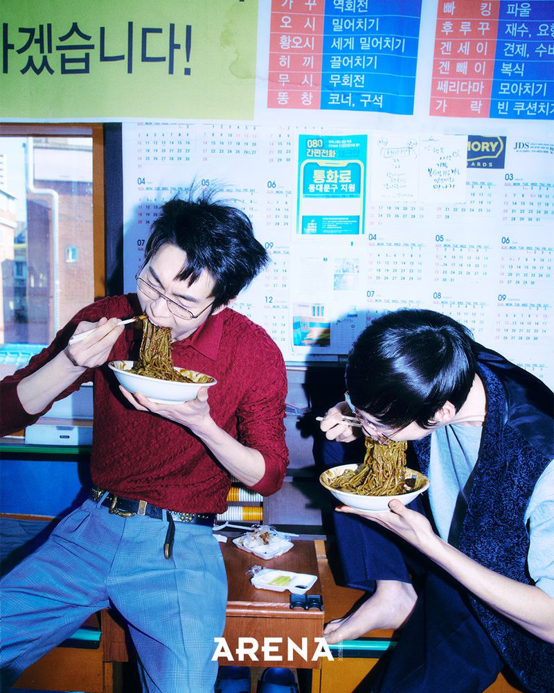 Two men eating noodles with chopsticks indoors with calendar posters on the wall for Arena Homme Plus Korea by Less Kim Tae Kyun
